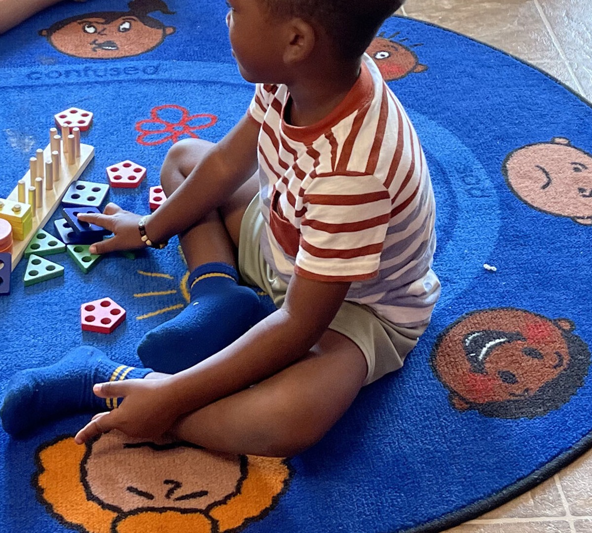 Child sitting on the play rug stacking colorful wooden shape blocks