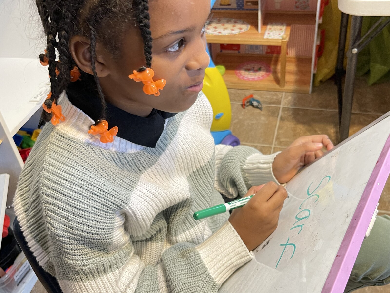 Child writing her name on a whiteboard easel at Peace & Nevaeh Childcare